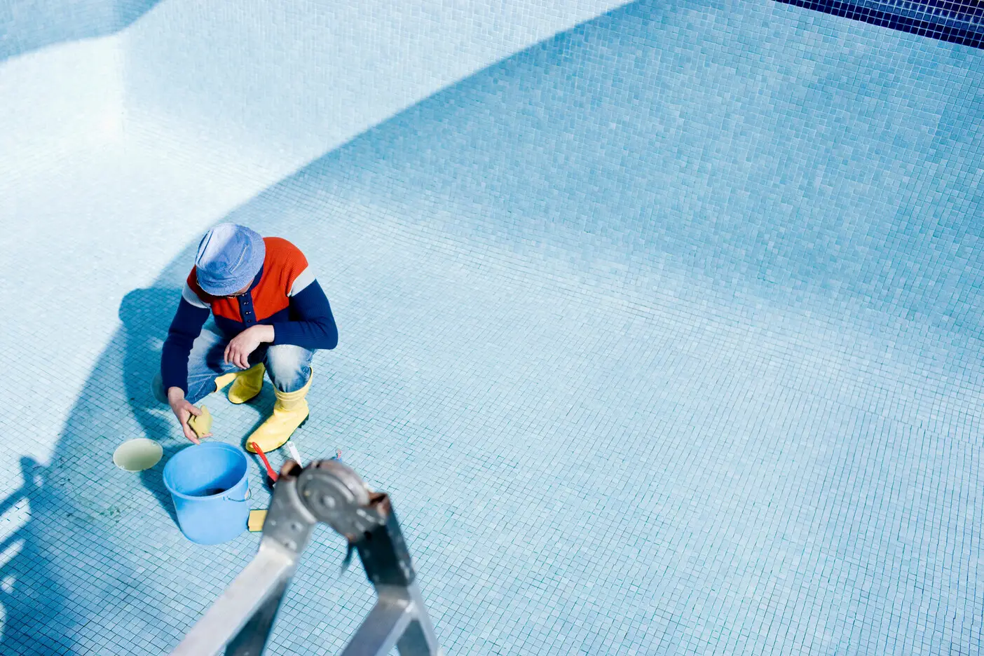 Person cleaning an empty swimming pool with bucket.